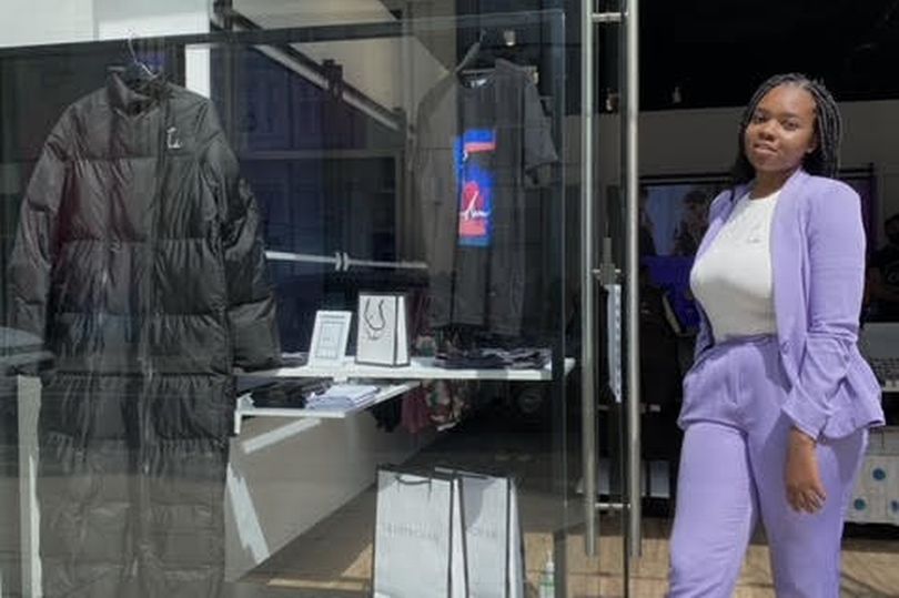 Cherise is wearing a purple suit and standing outside her new shop.